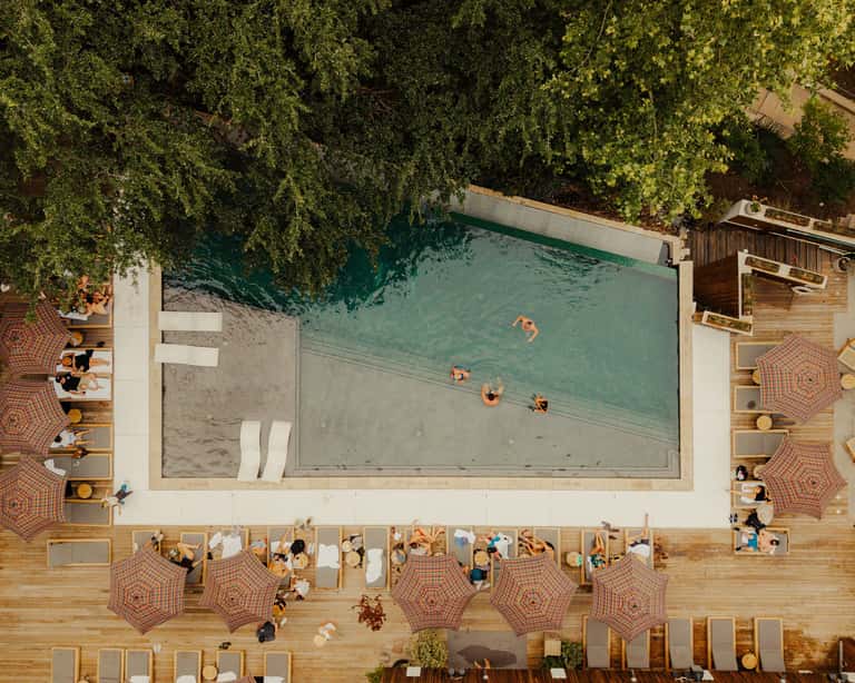Overhead view of resort pool with swimmers, umbrellas, and wooden deck surrounded by lush green trees