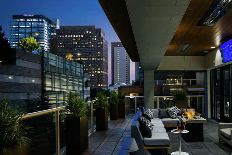 Hotel rooftop terrace at evening with fire pit, seating, city skyline view, and warm ambient lighting