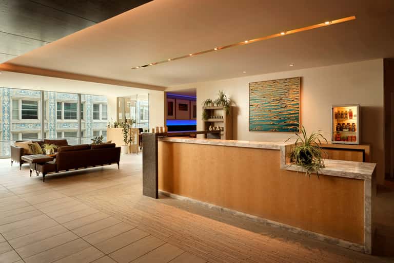 Modern hotel lobby with reception desk, lounge seating, and city views through floor-to-ceiling windows