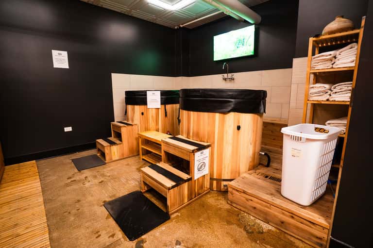 Wooden hot tub and cold plunge pool spa area with white towel storage and black accent walls