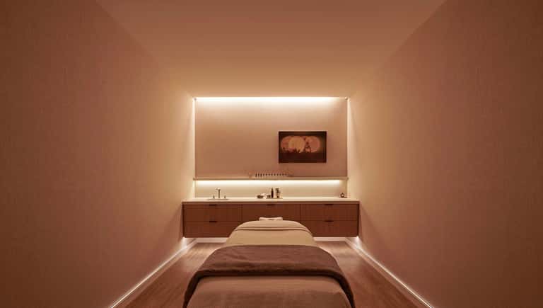 Minimalist massage room with warm lighting, wooden vanity, and comfortable massage bed