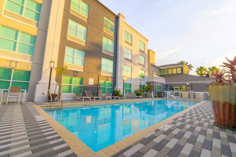 Resort swimming pool with lounge chairs, palm trees, and modern hotel building at golden hour