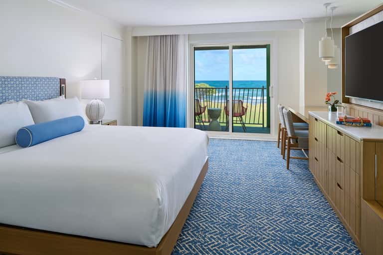 Modern hotel bedroom with ocean balcony view, blue ombre curtains, and contemporary furnishings
