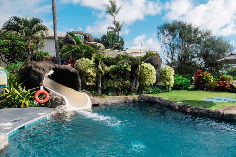 Resort pool with white slide, rock formations, tropical landscaping, and manicured lawn