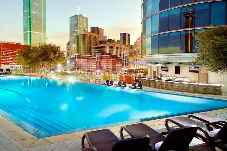 Urban rooftop pool at dusk with city skyline and lounge chairs