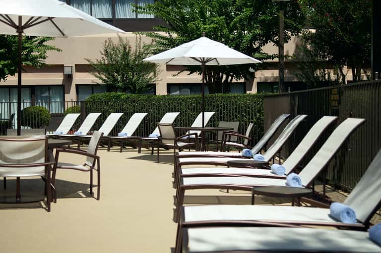 Resort pool deck with lounge chairs, umbrellas, and palm trees overlooking building facades