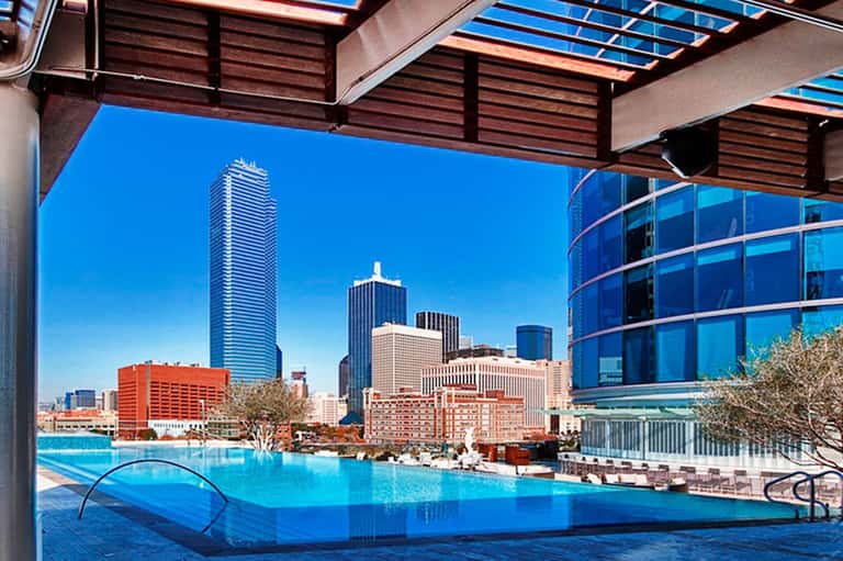 Indoor luxury pool with city skyline view through floor-to-ceiling windows and wooden ceiling details