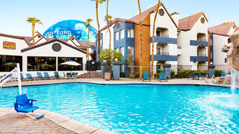 Resort pool with blue water, palm trees, white and blue residential buildings and mountain backdrop