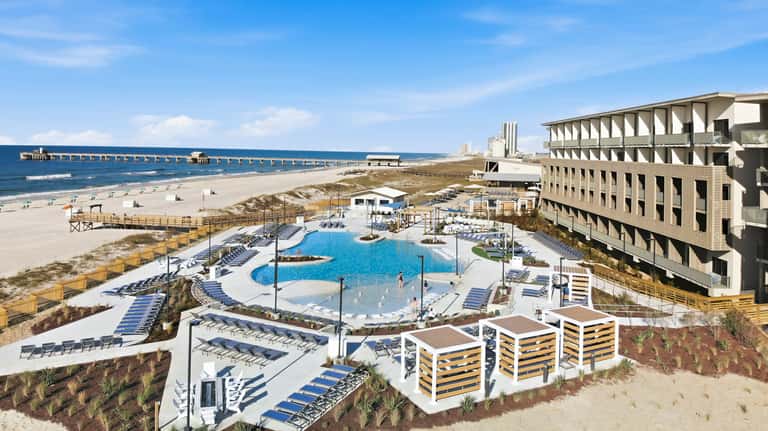 Resort pool area with blue water feature, surrounding lounge chairs, beach access, and hotel building