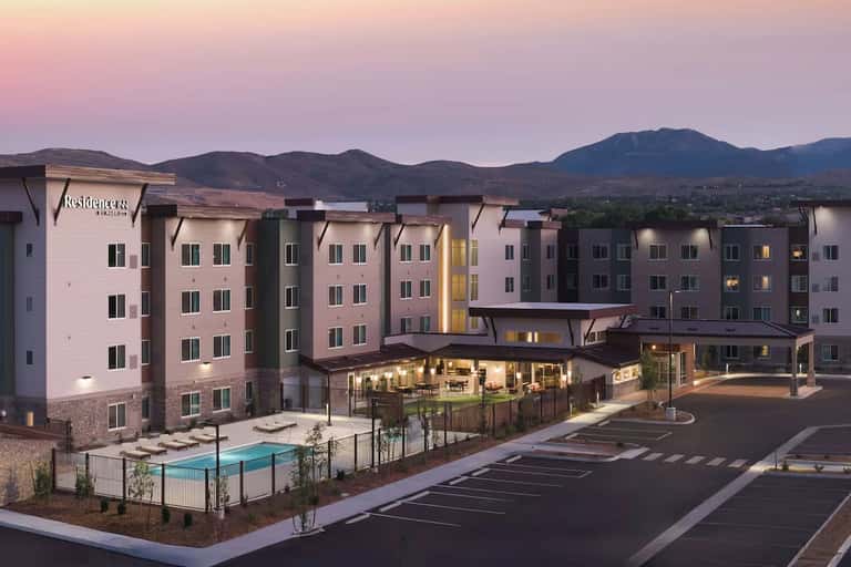 Residential complex at twilight with illuminated lobby, pool area, and mountain backdrop against pink sky