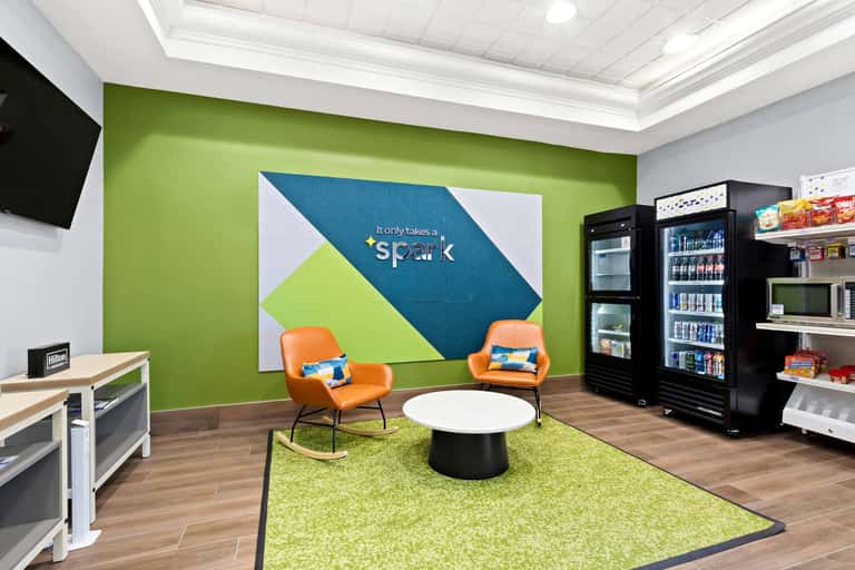 Bright lounge area with lime green accent wall, orange chairs, white round table, and beverage coolers