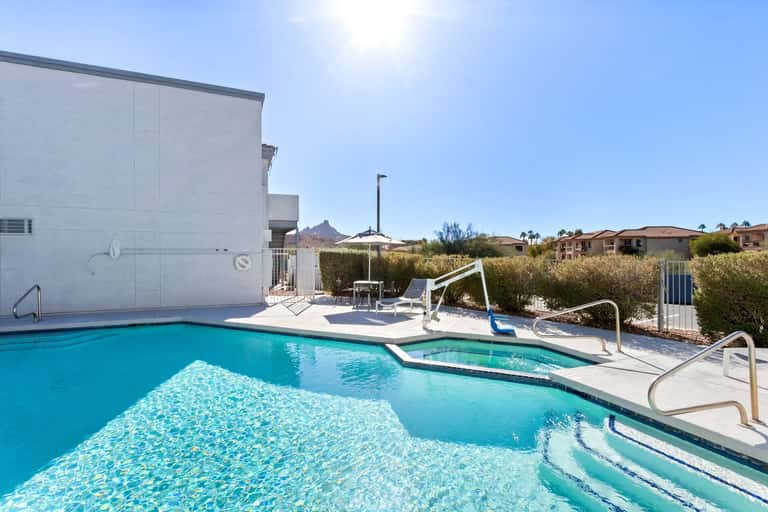 Outdoor pool and hot tub with desert landscape and mountain views under clear sky