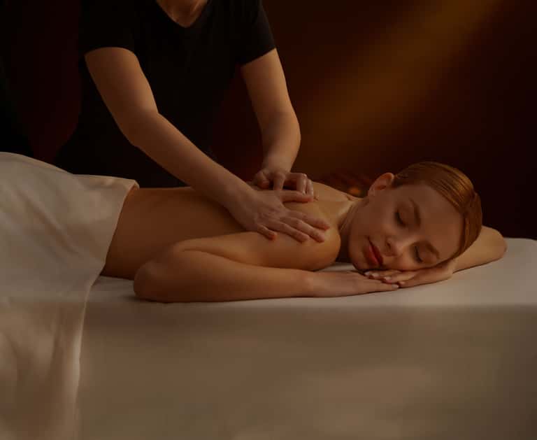 Spa therapist performing back massage on relaxed client lying face down on massage table