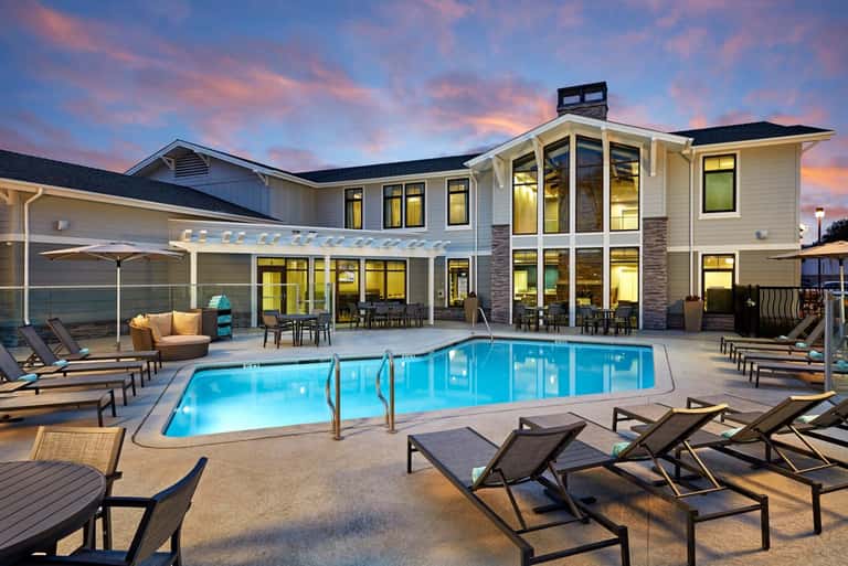Contemporary house with resort-style pool, lounge chairs, and covered patio at sunset