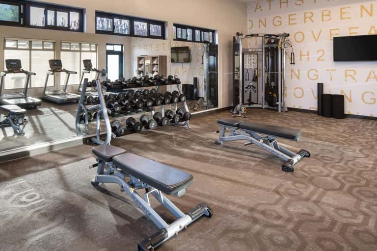 Upscale fitness facility with cardio equipment, free weights, benches, and motivational wall graphics