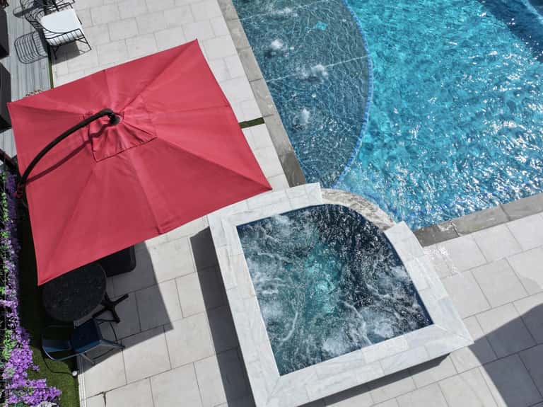 Red cantilever umbrella beside rectangular pool with white patio decking and spa jets