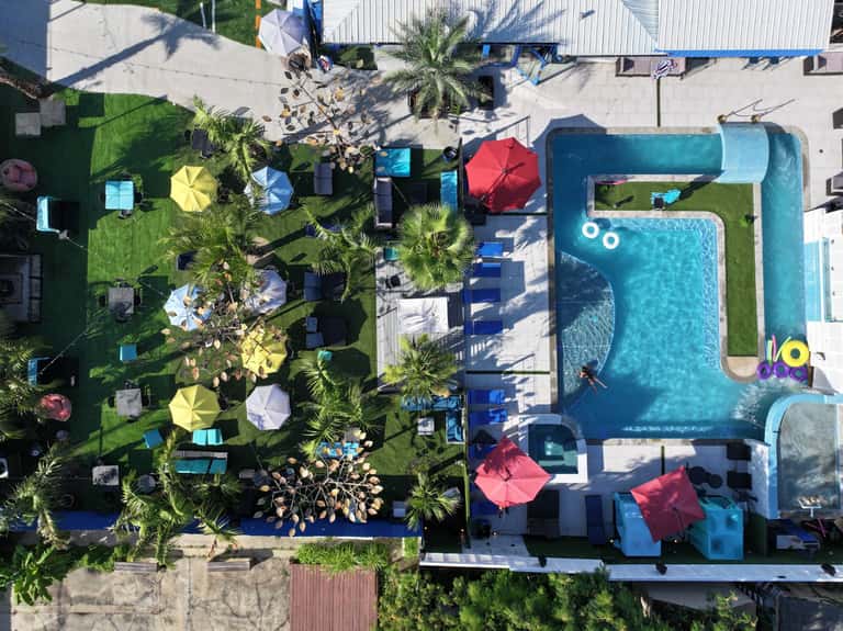 Aerial view of resort with turquoise pool, lush landscaping, colorful umbrellas, and lounge areas