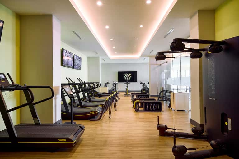 Modern fitness center with yellow accent walls, cardio equipment, and cycling bikes