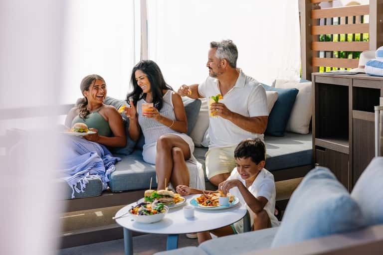 Family of four enjoying beverages and food together on a gray couch in a bright living room