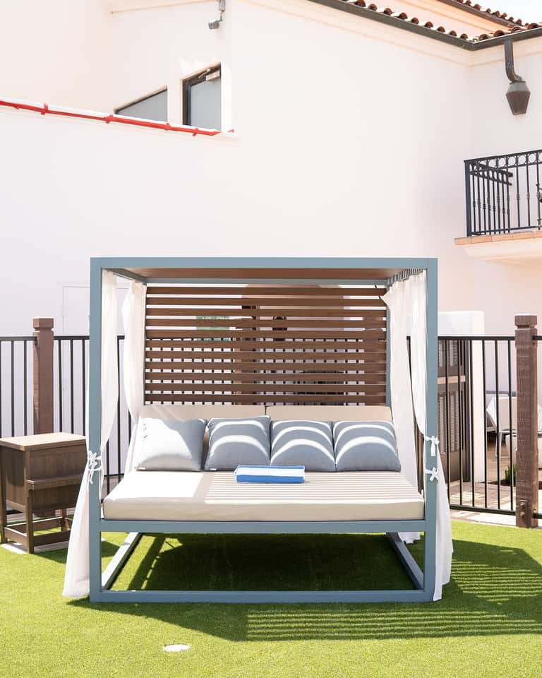 Elegant canopy daybed with striped blue and white pillows on manicured lawn with building backdrop