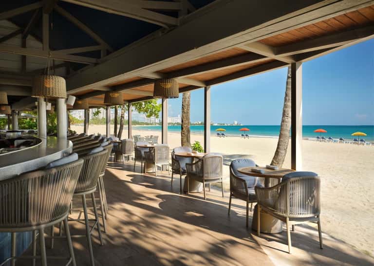 Covered beachfront pavilion with woven pendant lights, lounge seating, and ocean view