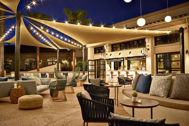 Elegant outdoor patio at night with illuminated sail shade, lounge seating, bar counter, and string lights