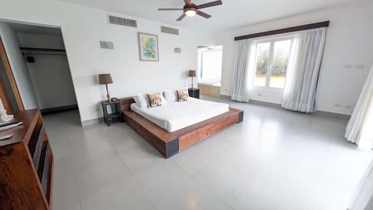 Spacious master bedroom with wooden platform bed, white tile floor, and garden views