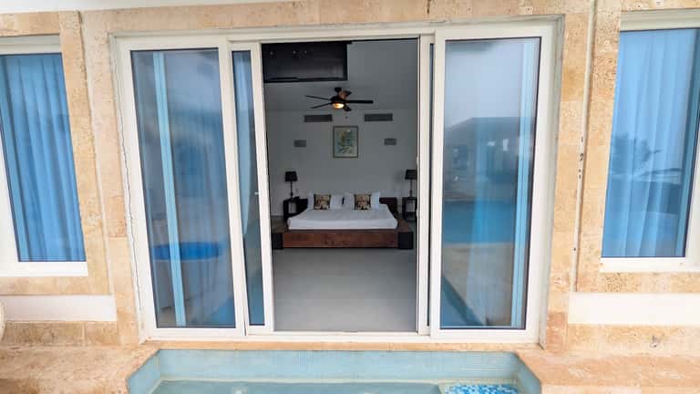 Beachfront bedroom with sliding glass doors opening to ocean views and small pool
