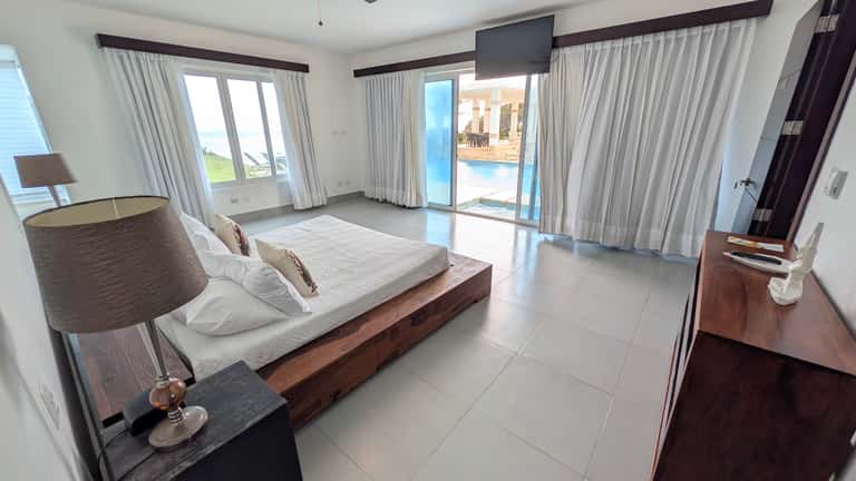 Modern waterfront bedroom with wooden bed, multiple glass doors, and water views