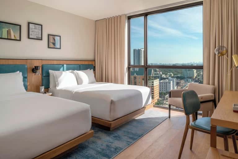 Spacious hotel room with two queen beds, panoramic city views, and contemporary wooden furnishings