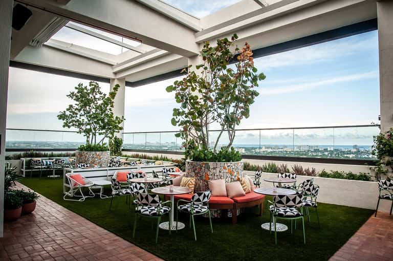 Rooftop terrace with modern seating, potted plants, glass railings, and expansive city skyline views