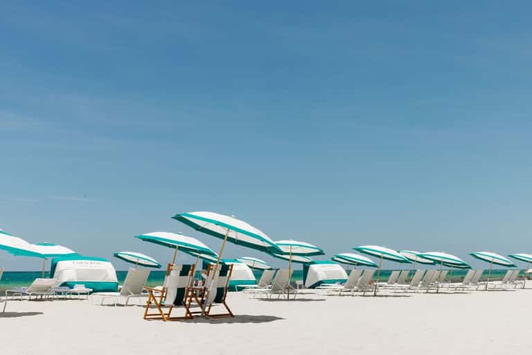 Sandy beach with rows of teal and white striped umbrellas and lounge chairs under clear sky