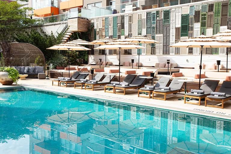 Resort pool with lounge chairs, umbrellas, and modern building facade