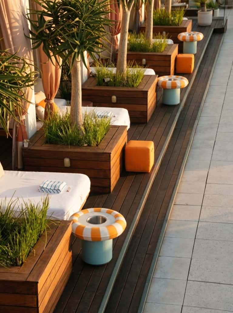 Row of luxury cabana daybed stations with brown wood planters, orange seating, and white linens