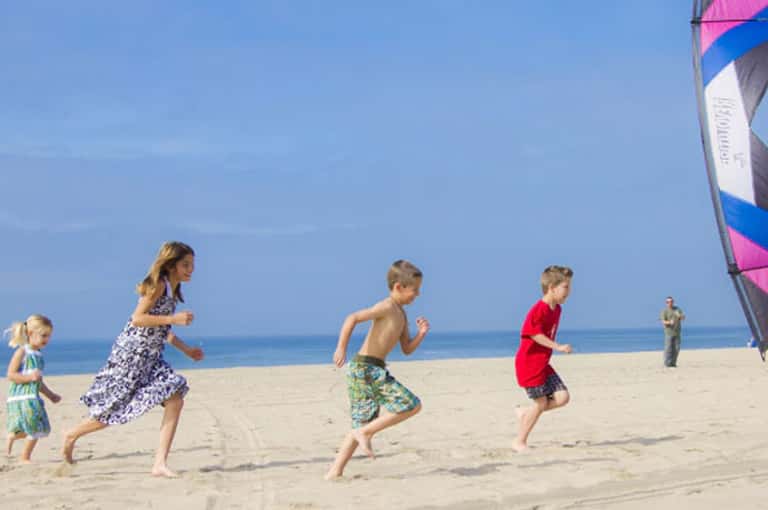 Children running on sandy beach with colorful kite in background