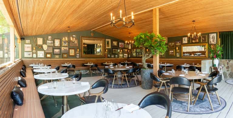 Restaurant interior with wooden ceiling, gallery wall artwork, round tables, and black chairs