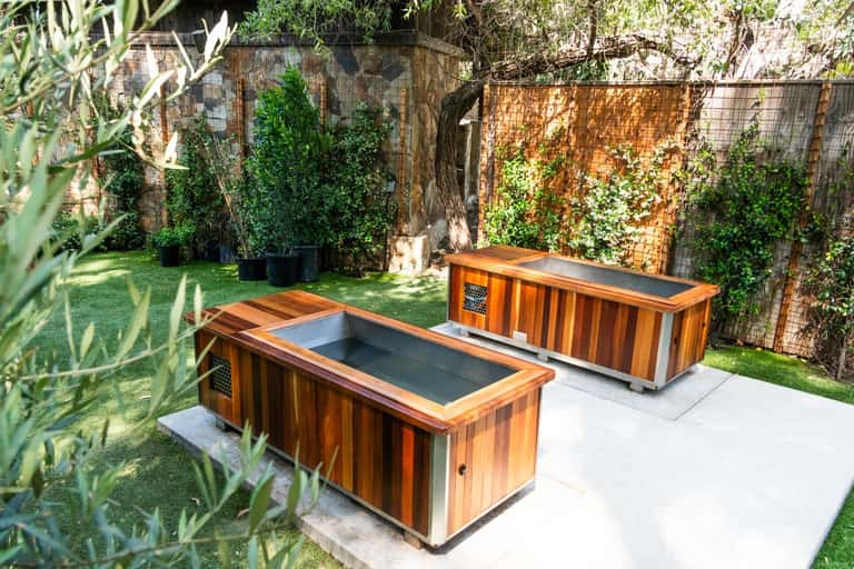 Two wooden spa tubs in a landscaped garden courtyard with ivy-covered walls and green lawn
