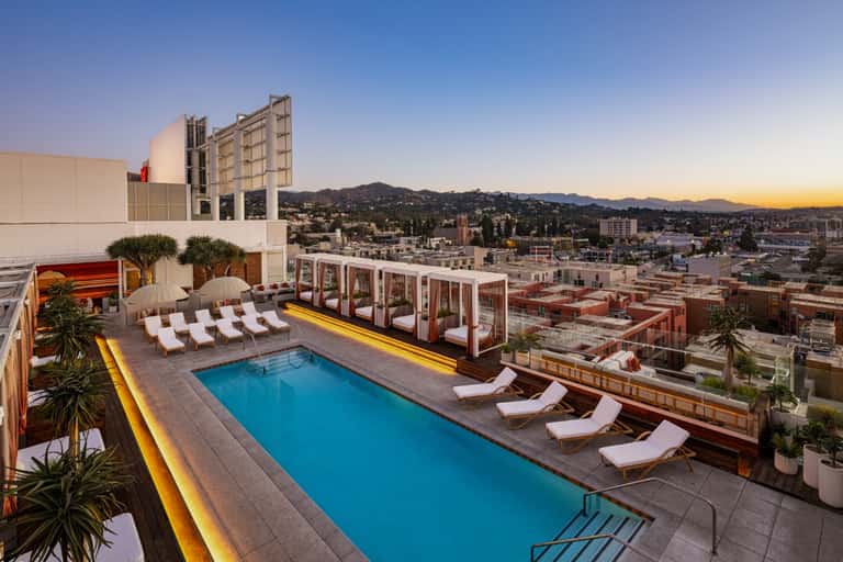 Rooftop pool deck at sunset with loungers, cabanas, and mountain city views