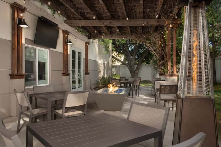 Elegant outdoor patio with fireplace, dining tables, lounge chairs, and string lights under wooden pergola