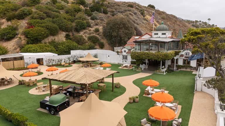 Hillside resort grounds with multiple orange umbrellas, wooden pergola, artificial turf, and coastal vegetation