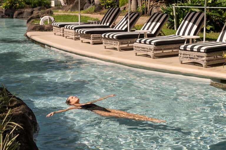 Lounge chairs with striped cushions beside clear lagoon pool with tropical vegetation and water features