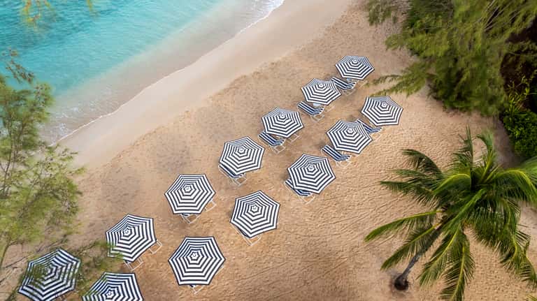 Overhead view of beach with rows of black and white striped umbrellas, sand, and turquoise water