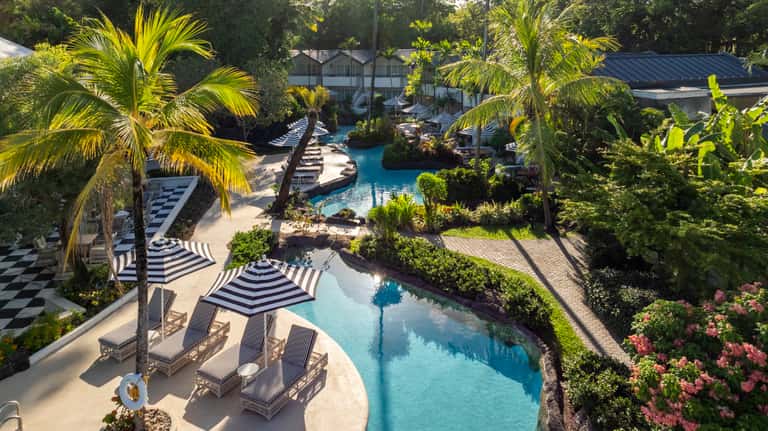 Overhead view of curved resort pools with black and white striped umbrellas and tropical landscaping