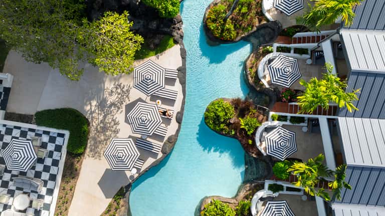 Top-down view of winding turquoise pool with hexagonal umbrellas, loungers, and resort buildings