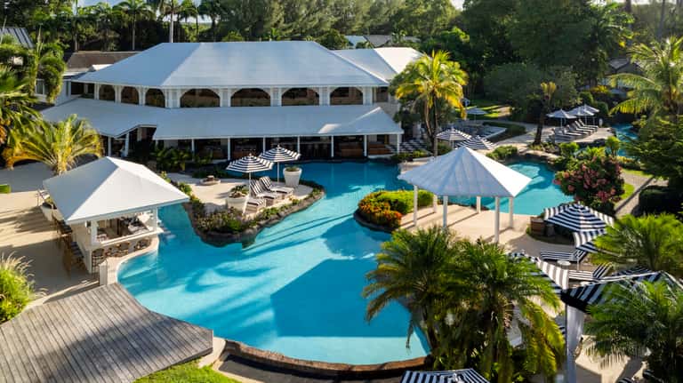 Aerial view of expansive resort complex with curved pools, white structures, and surrounding palm trees