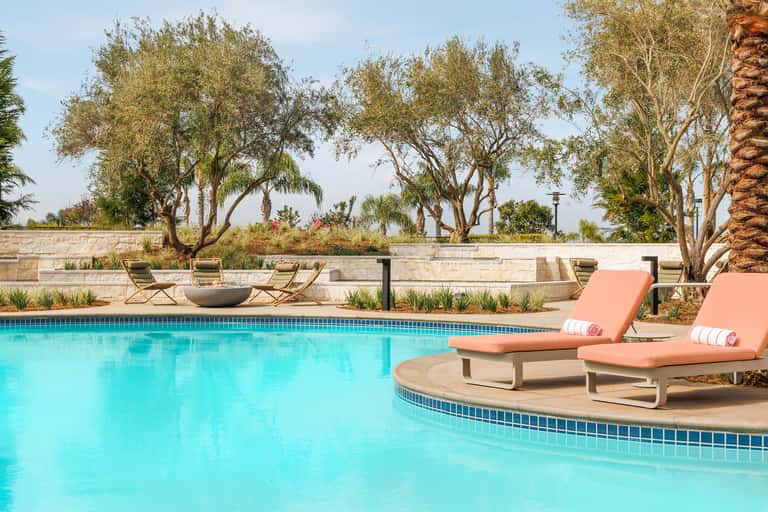 Resort pool with turquoise water, coral lounge chairs, mature trees, and stone wall backdrop at dusk