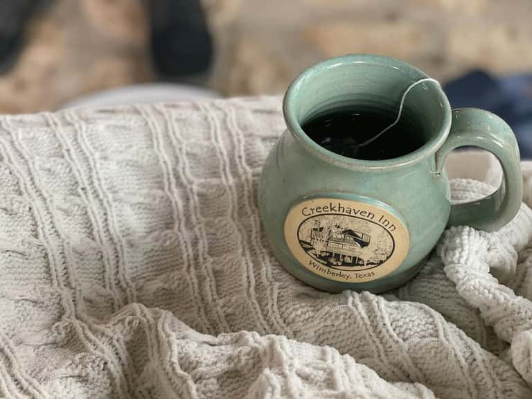 Green ceramic pitcher labeled 'Creekhaven Inn' resting on textured fabric and sand