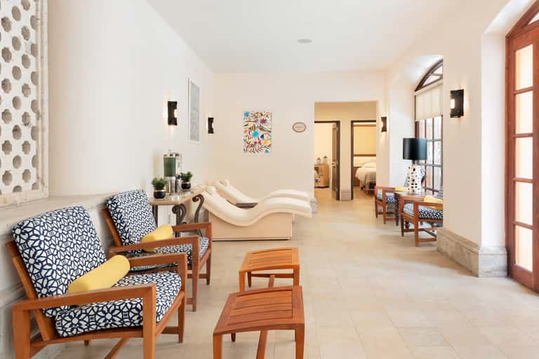 Bright spa waiting area with patterned chairs, archways, and doorways leading to treatment rooms