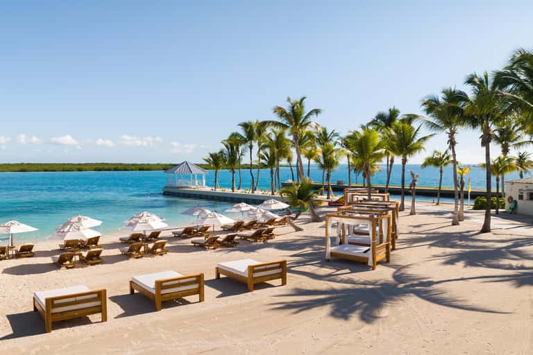 Tropical beach resort with white umbrellas, lounge chairs, palm trees, and turquoise ocean water