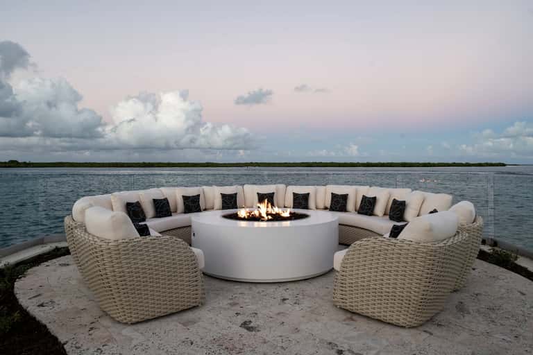 Curved woven lounge seating around fire pit overlooking calm water at dusk